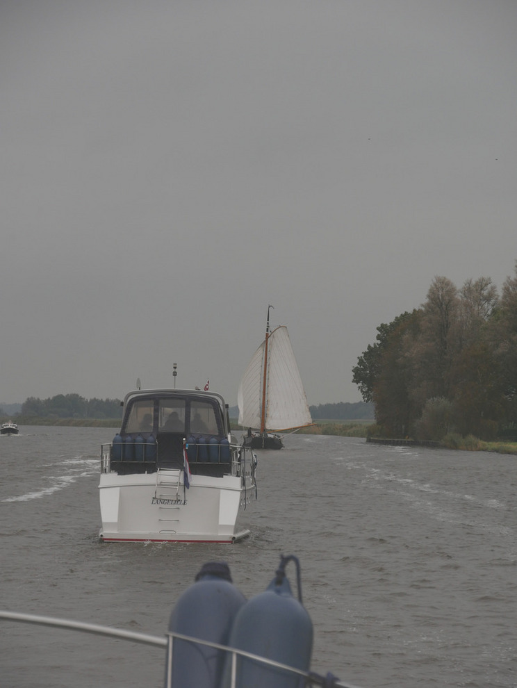 Eine Motorboot und ein Segelboot fahren durch eine graue trübe Landschaft.