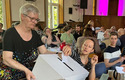 Das Bild zeigt eine Abstimmung im Kirchentag der Bremischen Evangelischen Kirche. Eine Frau steckt ihren Stimmzettel in eine Wahlurne.