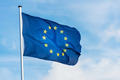 Das Foto zeigt eine im Wind wehende Europaflagge (blau mit einem Kreis goldener Sterne) vor einem blauen Himmel