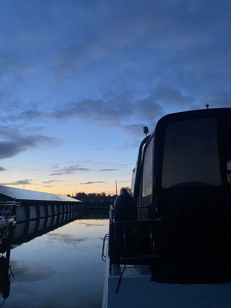 An einem Boot vorbeifotografiert sieht man über dem Hafen die Sonne aufgehen.