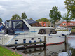 Ein Boot von der Seite fotografiert, das im Hafen festgemacht hat. Im Hintergrund sieht man weitere Boote und Häuser.